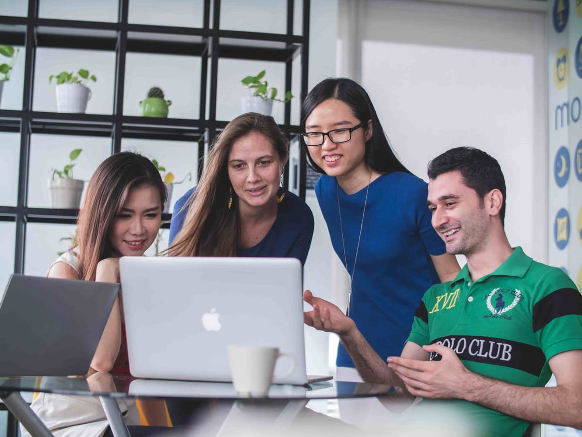 Business professionals collaborating around a laptop in a modern office setting, discussing project details and strategies